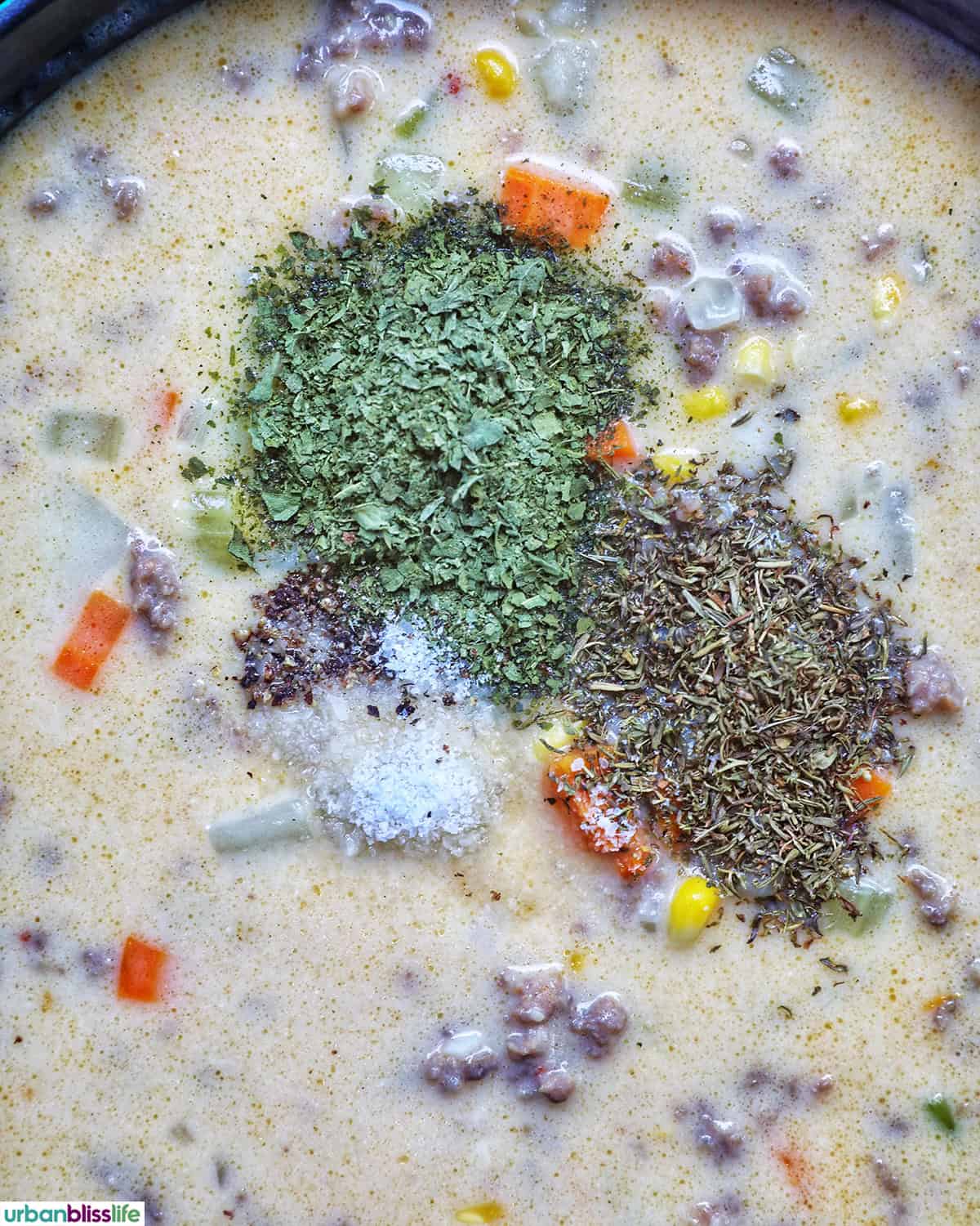 herbs added to top of carrots, celery, garlic, onions cooking in a pot.