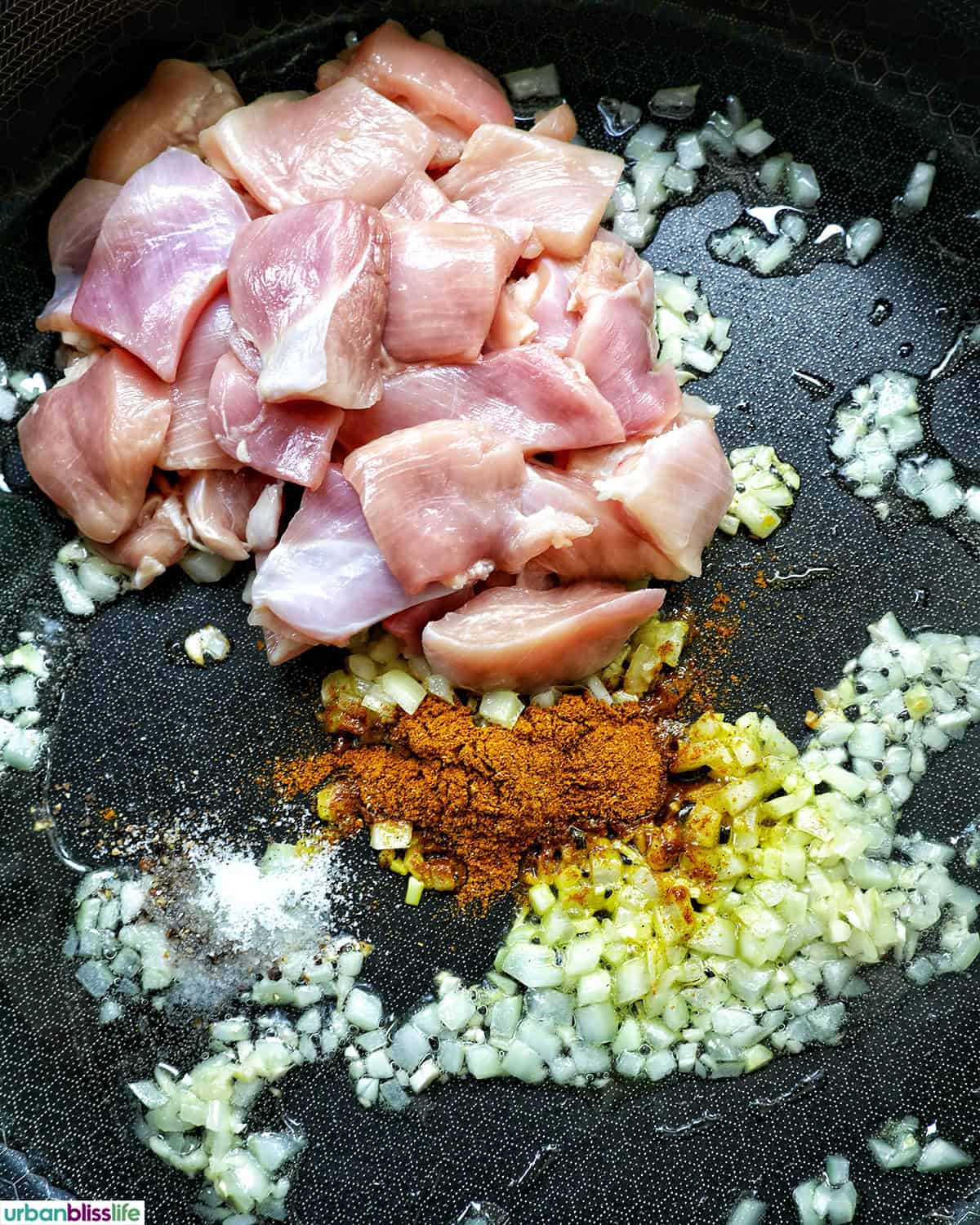 chicken, spices, onions and garlic in a pan.