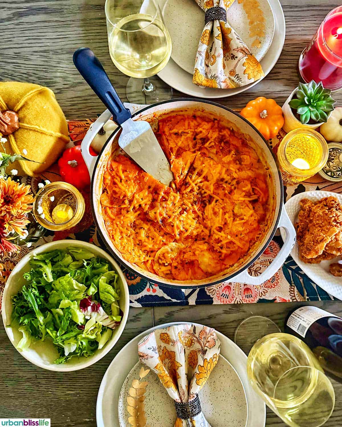 dinner table with sweet potato gratin, salad, chicken, glasses of wine, and fall decorations.