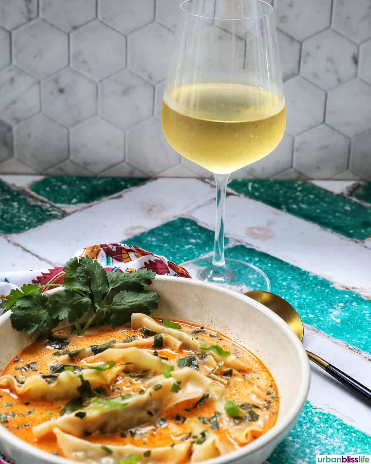bowl of Thai red curry dumpling soup with spoon and glass of wine.