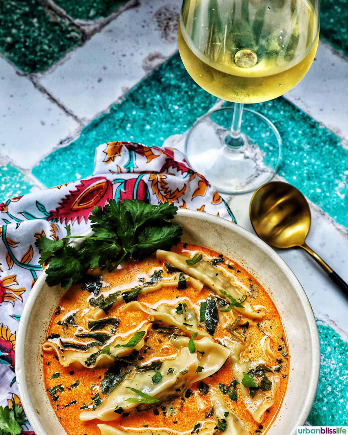 bowl of Thai red curry dumpling soup with spoon and glass of wine.