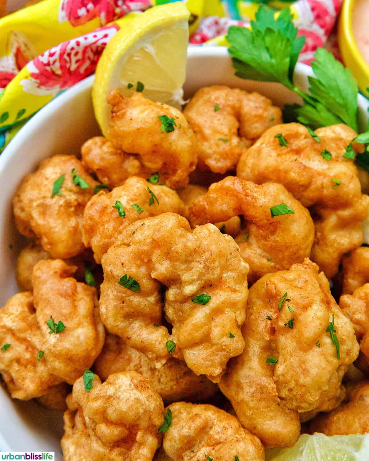 beer battered shrimp in a bowl with lemon slice and herbs.