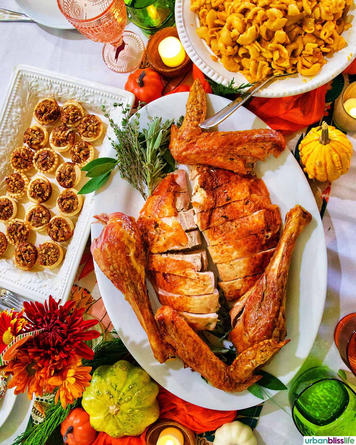Friendsgiving Thanksgiving turkey on a table with mini pecan pies and butternut squash mac and cheese.