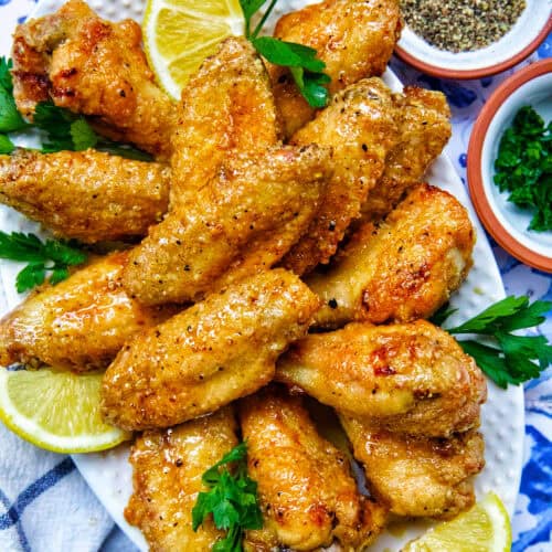 platter full of honey lemon pepper wings with parsley and lemon slices.