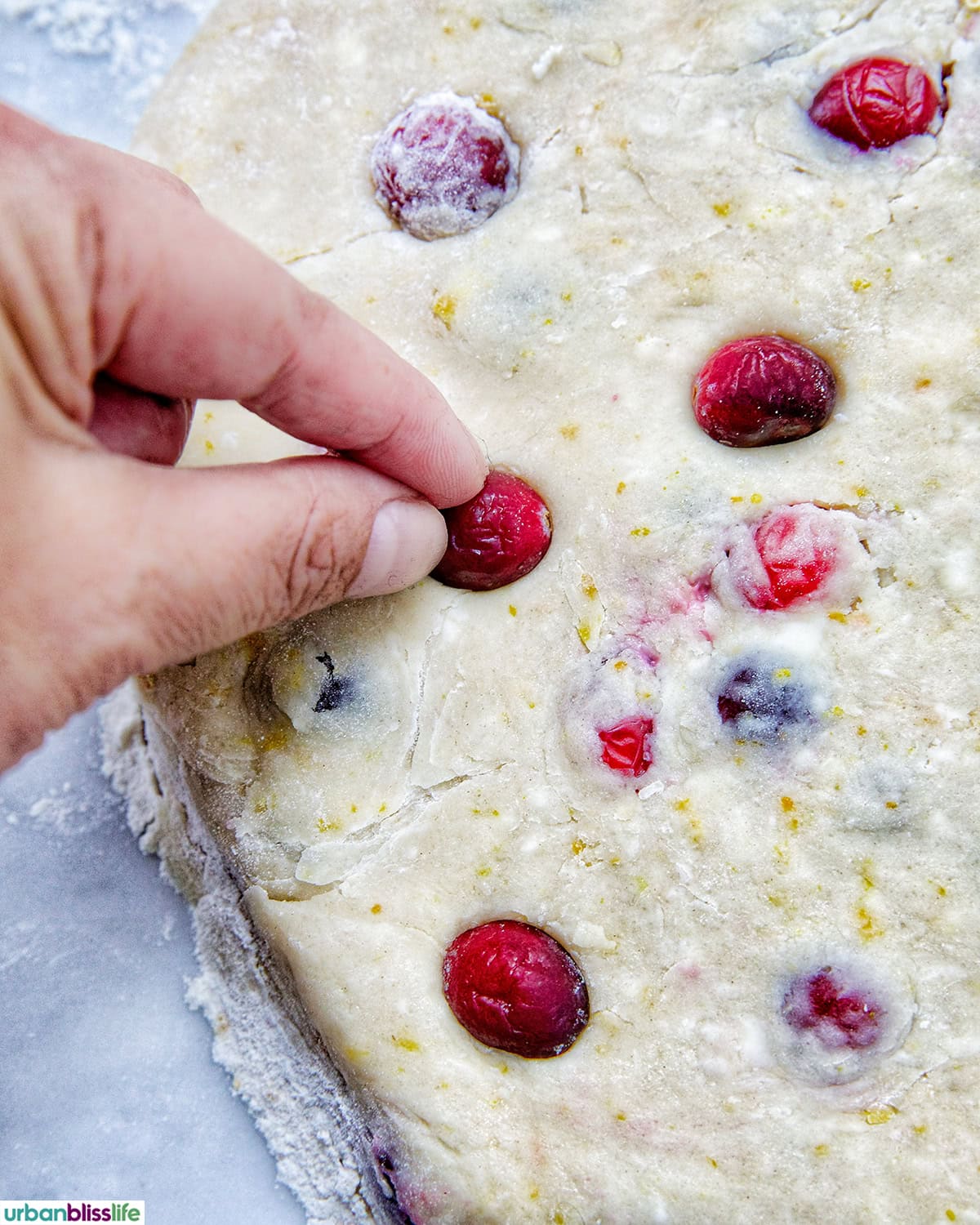 hand pressing a cranberry into orange cranberry scone dough.
