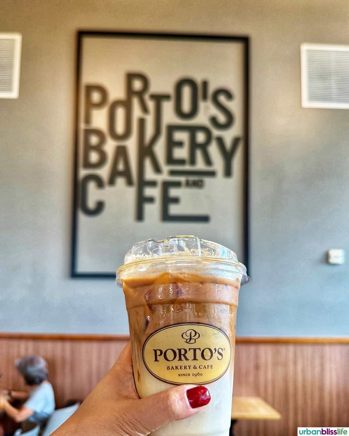 hand holding up an iced coffee in front of the Porto's Bakery Cafe sign in Buena Park, California.
