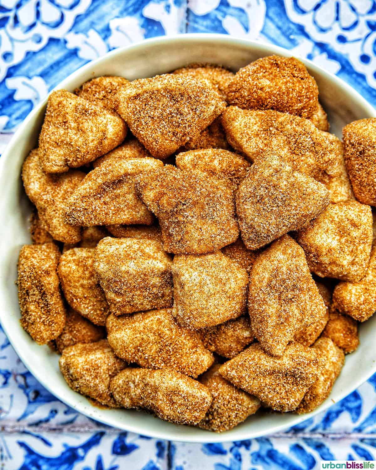 cut biscuit dough tossed in cinnamon spice mixture in a bowl.