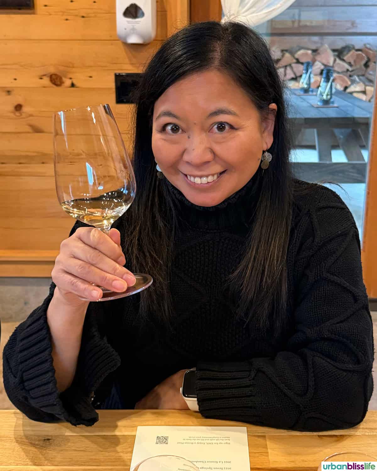 Marlynn holding a glass of white wine in Evening Land Vineyards wine tasting cabin.