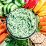 jar of vegan green goddess dressing in the center of sliced vegetables.