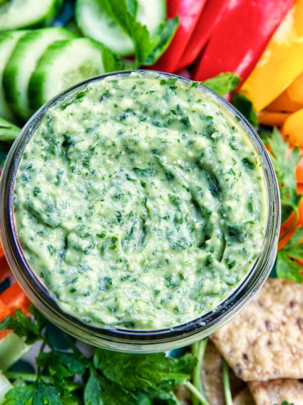 jar of vegan green goddess dressing in the center of sliced vegetables.