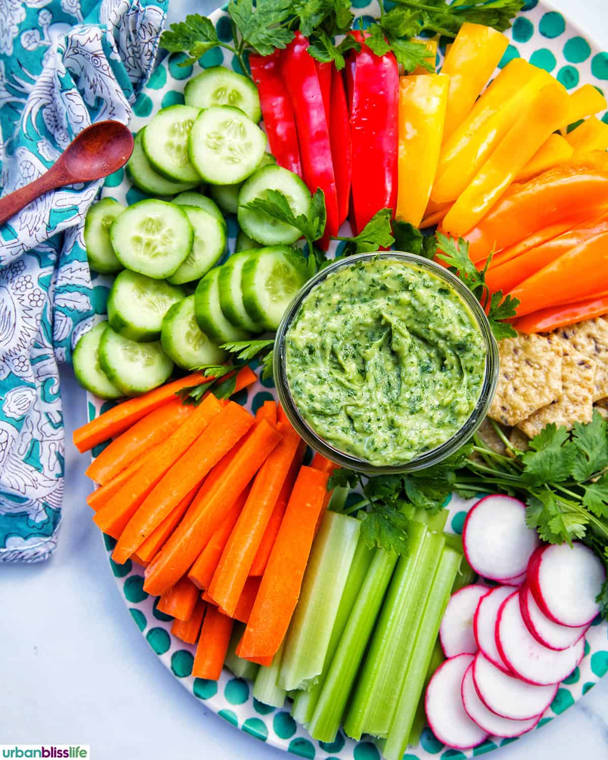jar of vegan green goddess dressing in the center of sliced vegetables.