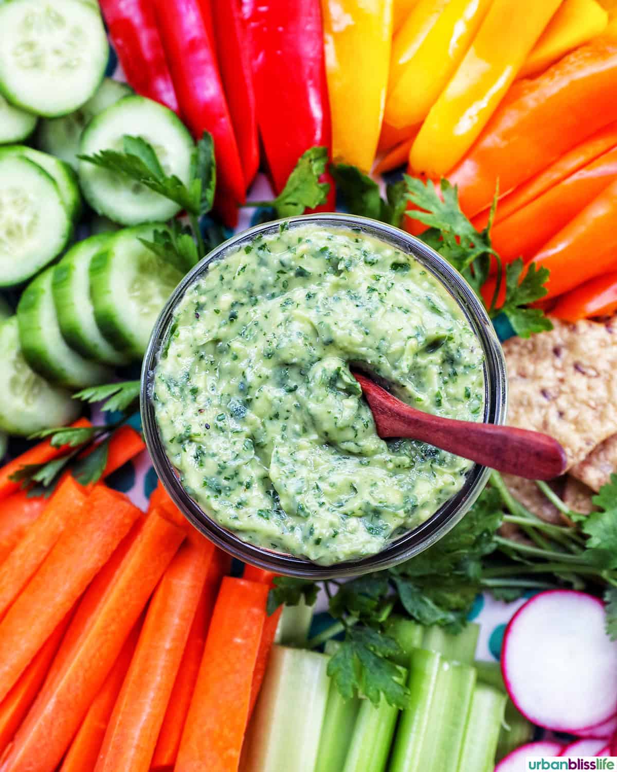 jar of vegan green goddess dressing in the center of sliced vegetables.