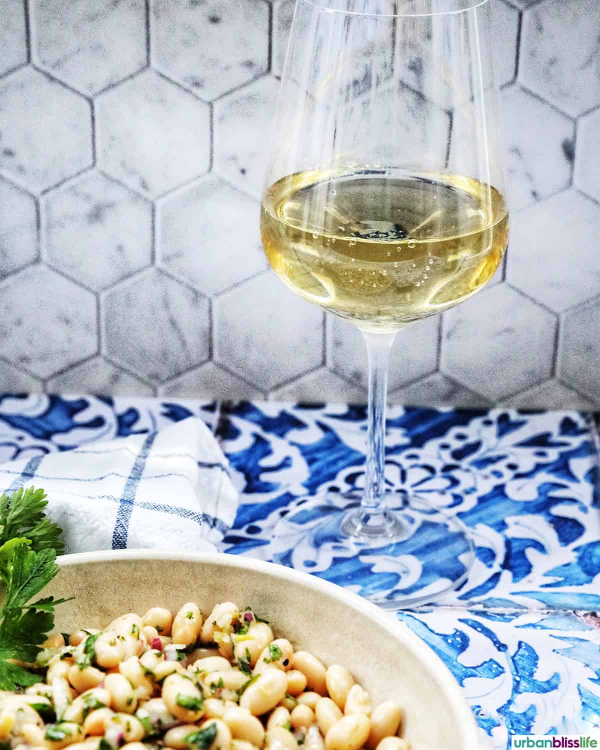 glass of white wine behind a bowl of white bean salad.