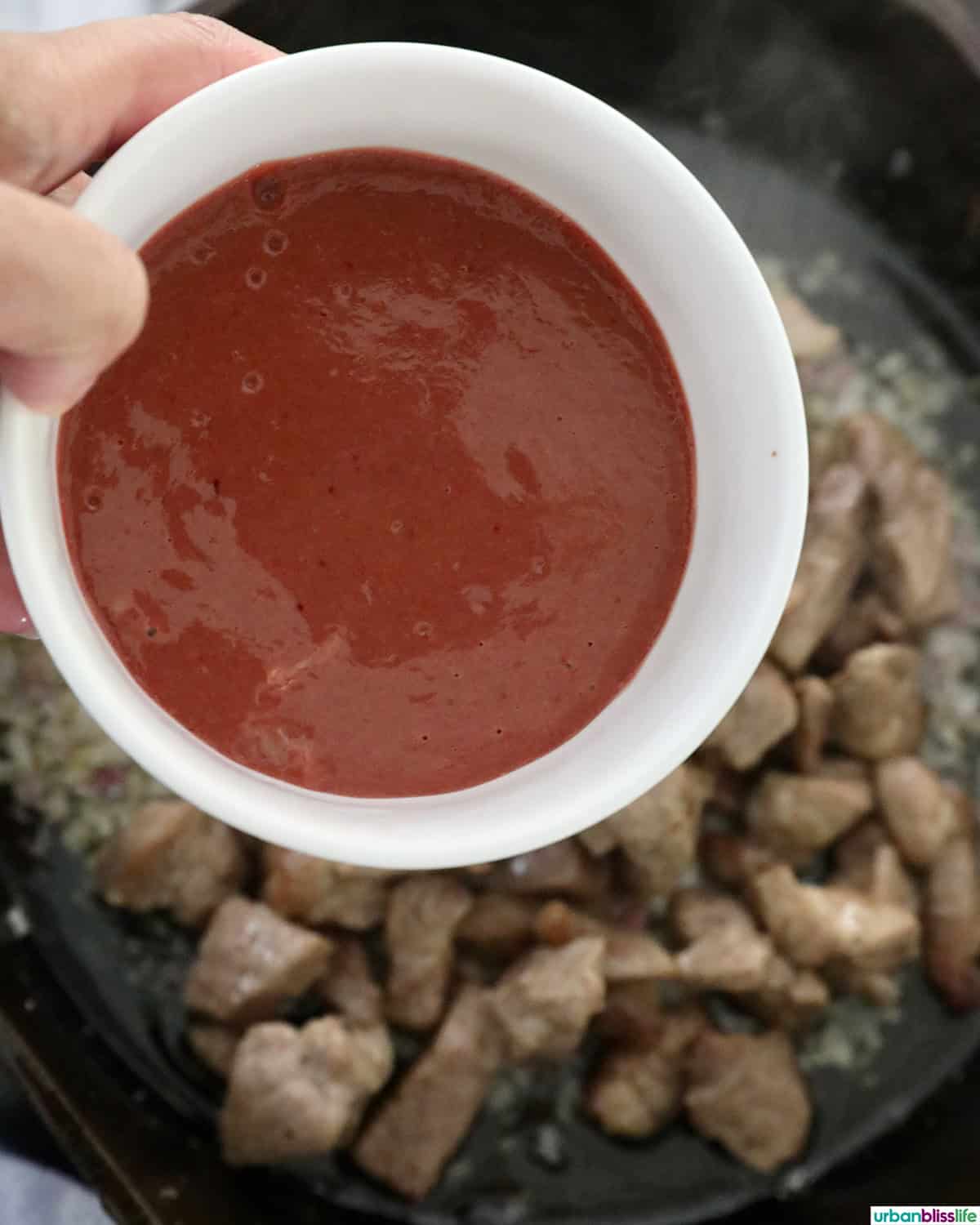 hand with a bowl of chicken livers over pan of Filipino pork sisig.