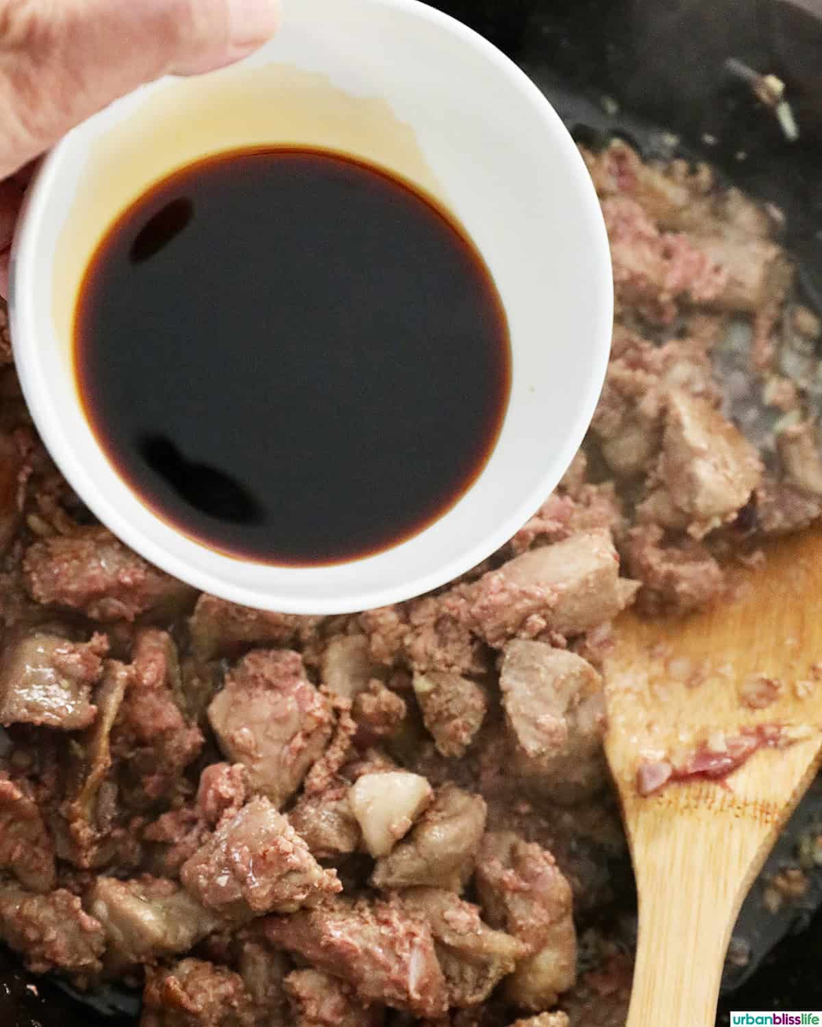 hand holding a bowl or sauce over Filipino pork sisig.