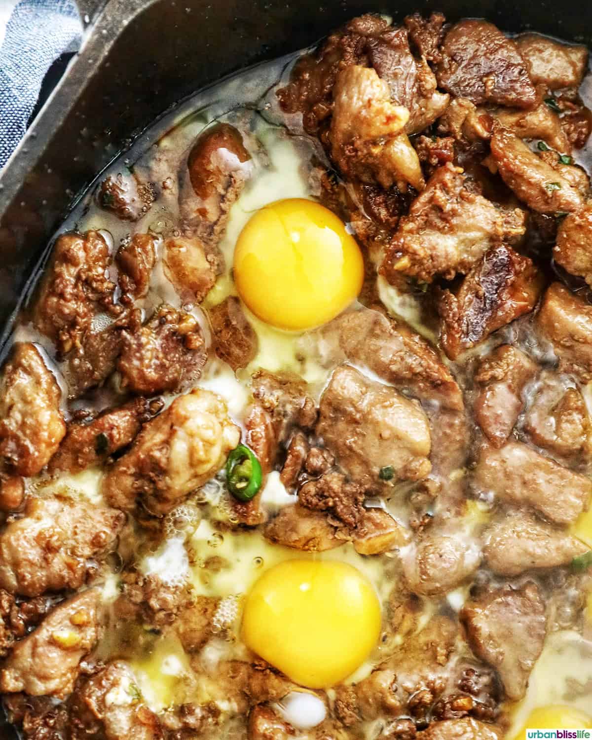 eggs over Filipino pork sisig cooking in a pan.