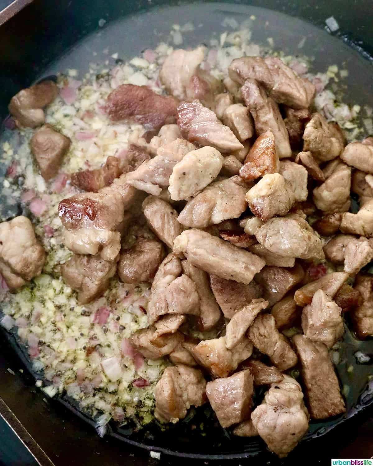 pork and aromatics cooking in a pan.