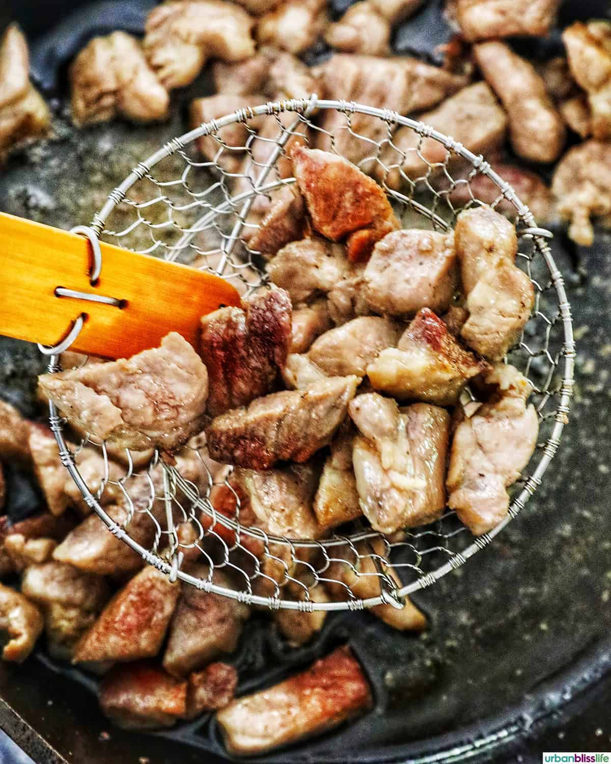 spider strainer with pork pieces over a pan of pork.