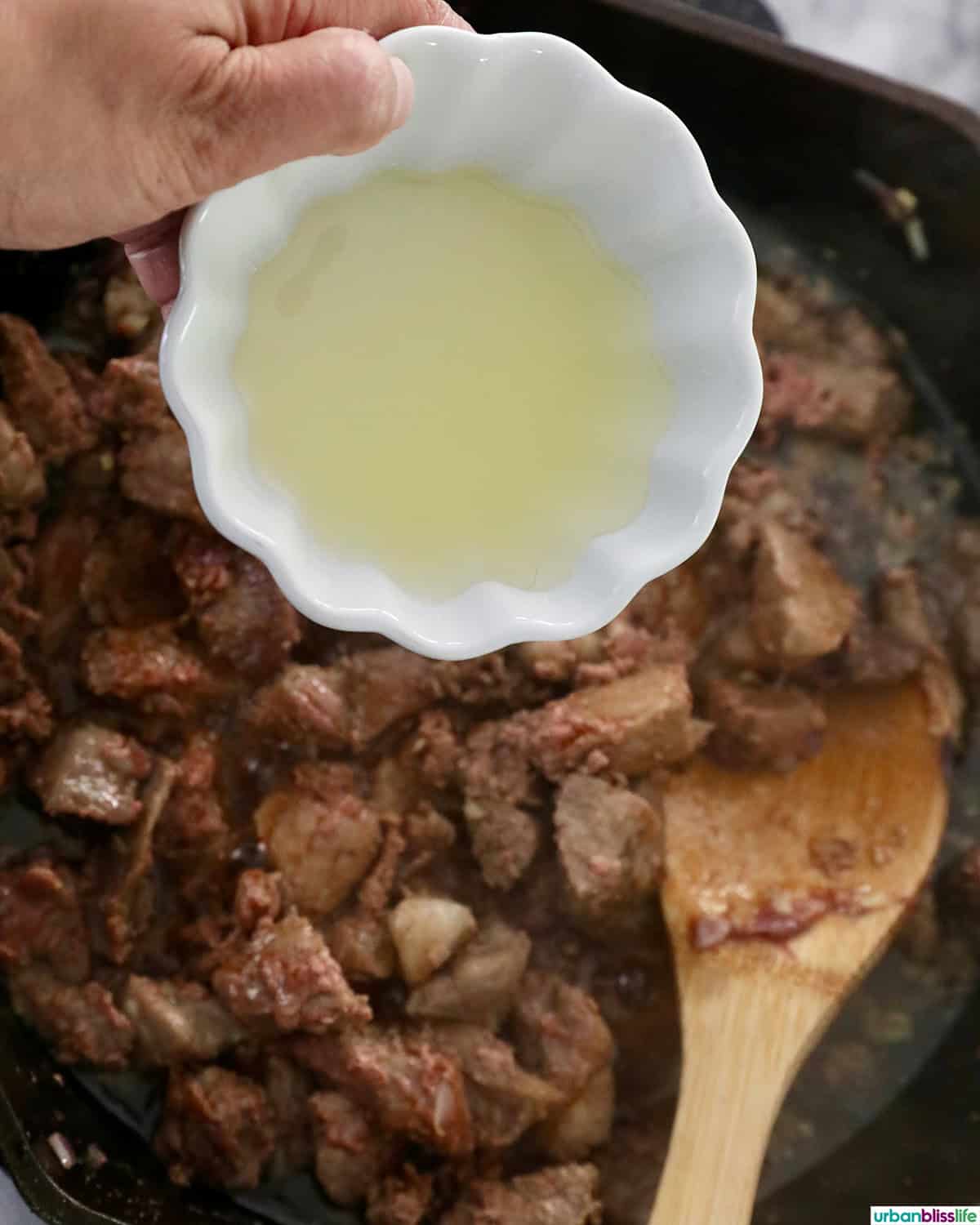 hand pouring liquid into pan of Filipino pork sisig.