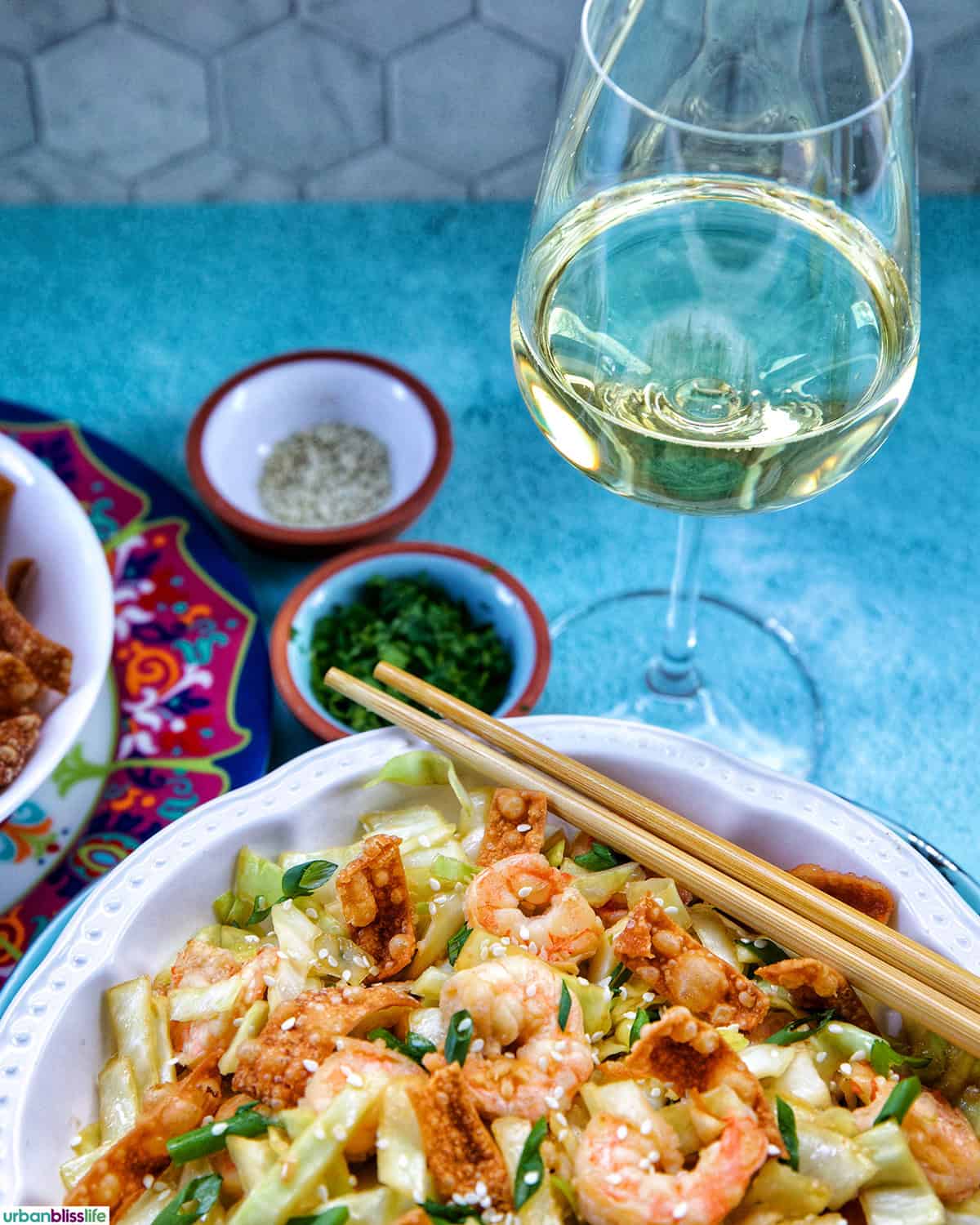bowl of cabbage and shrimp stir fry with chopsticks and a glass of white wine.