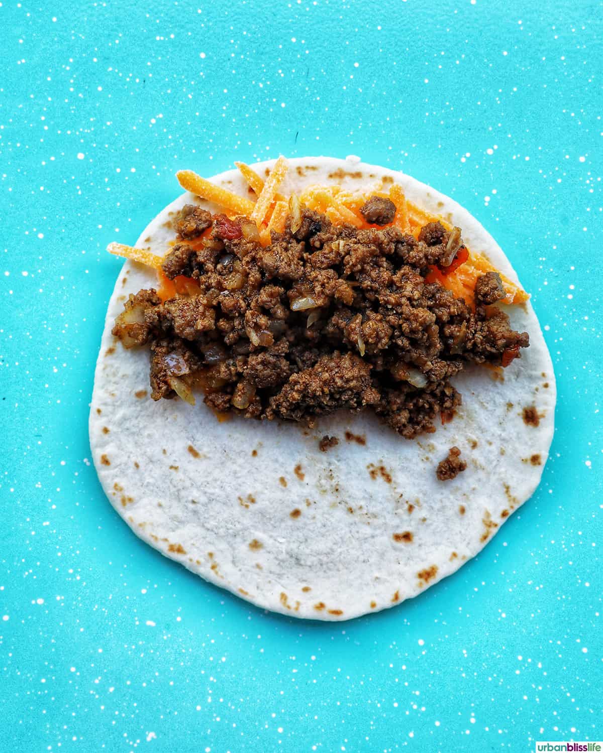 shredded cheese and ground beef on a tortilla.