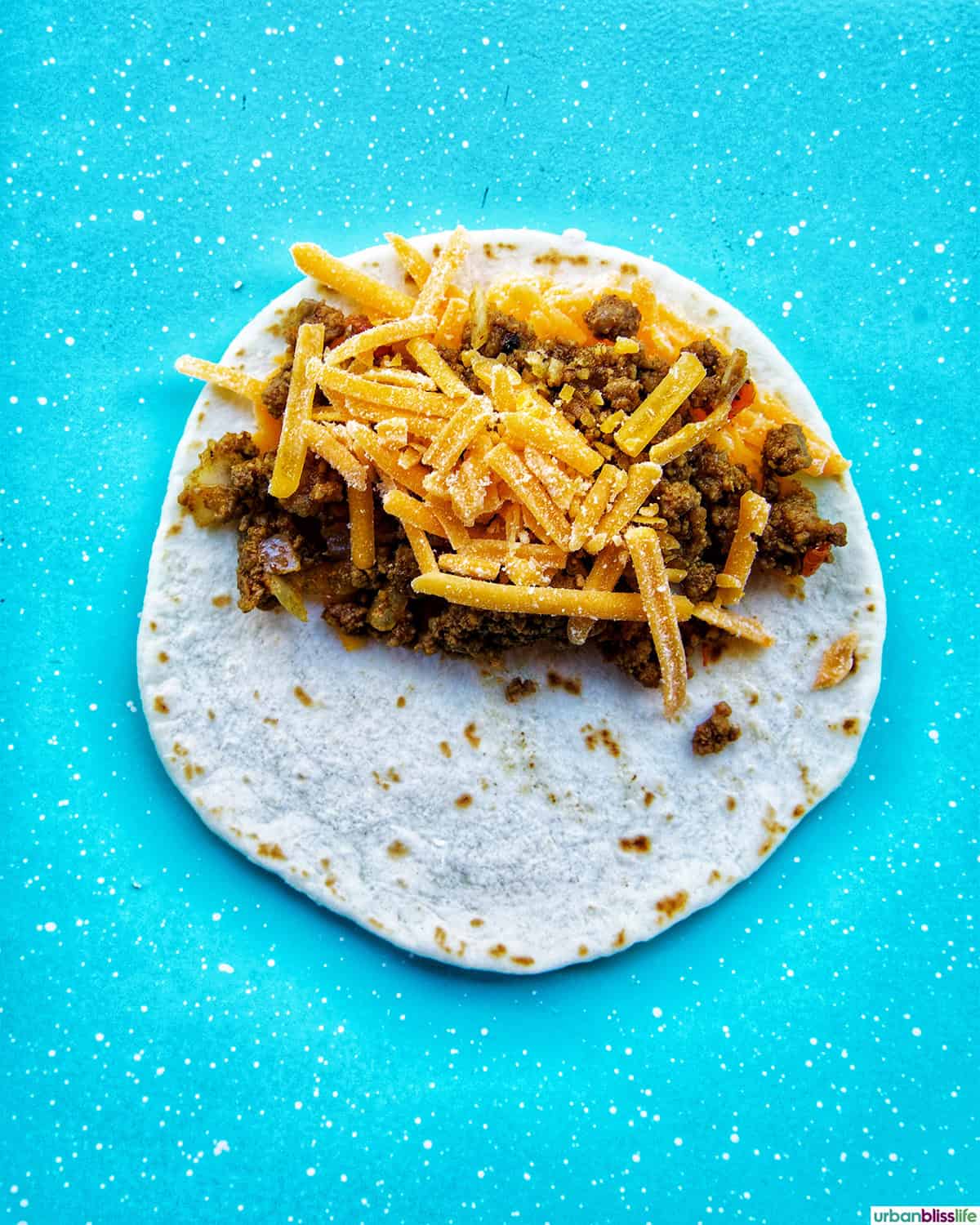 shredded cheese and ground beef on a tortilla.