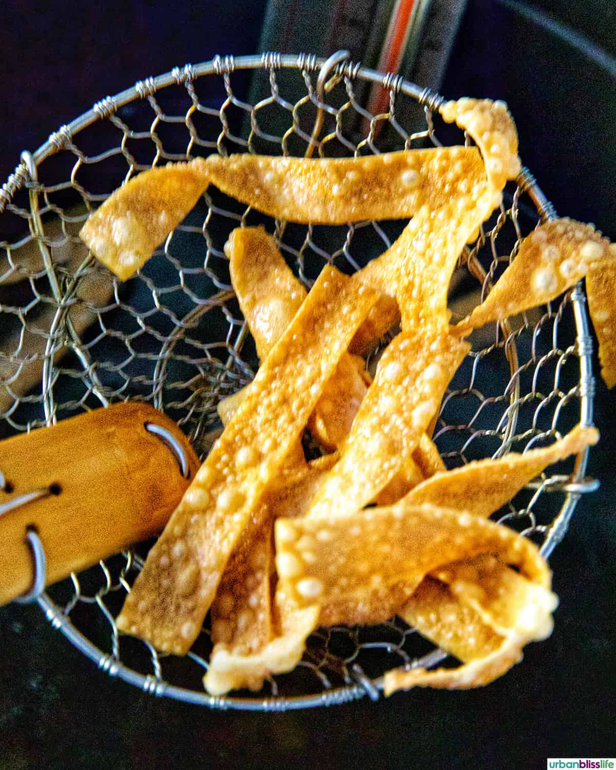 Fried Wonton Strips lifted in a spider strainer.