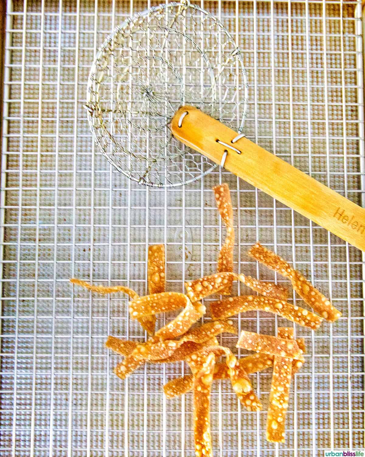 Fried Wonton Strips on a wire rack with a spider strainer.