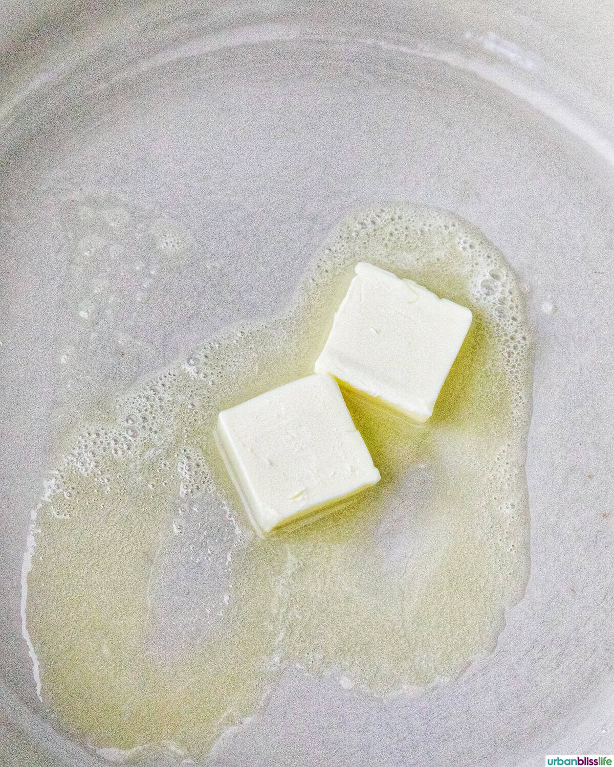 two pats of butter melting in a skillet.