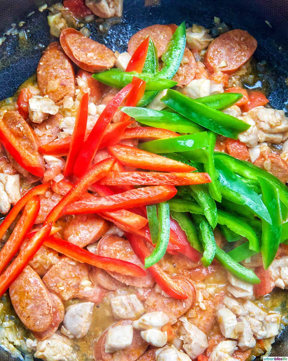 green and red bell peppers over Chorizo de Bilbao, chicken, aromatics in a skillet.