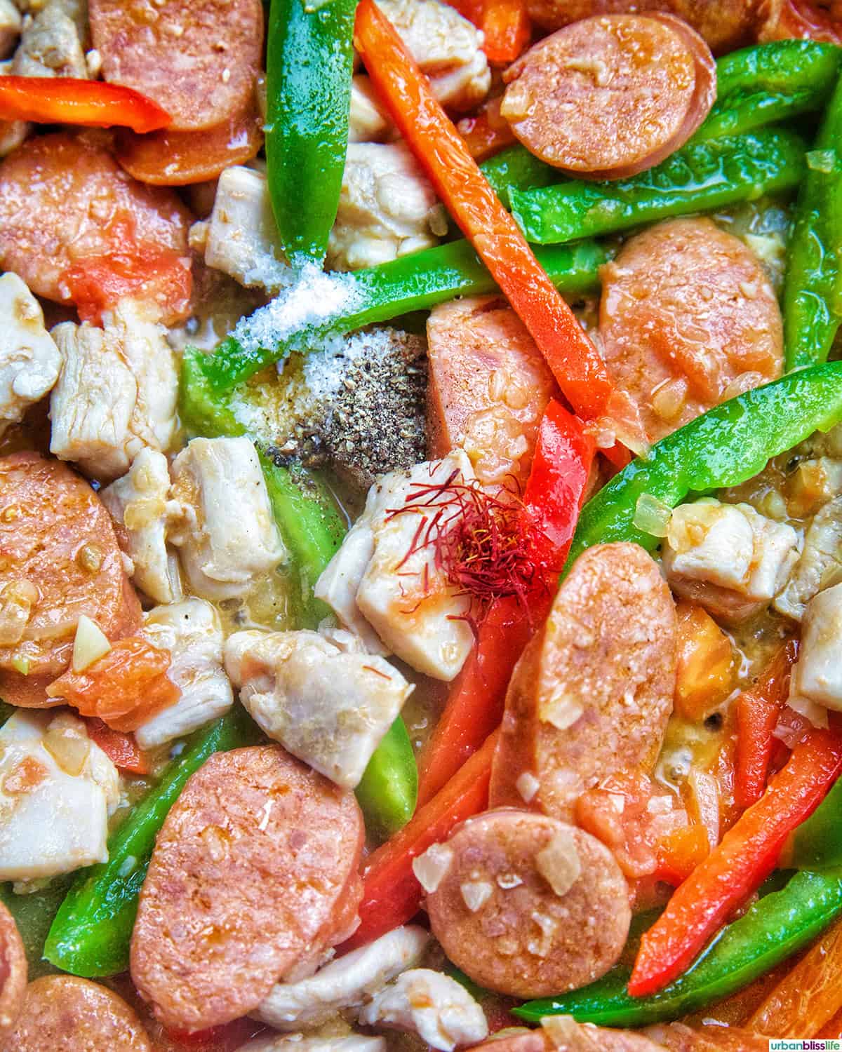 Chorizo de Bilbao, threads of saffron, bell peppers and chicken in a skillet.