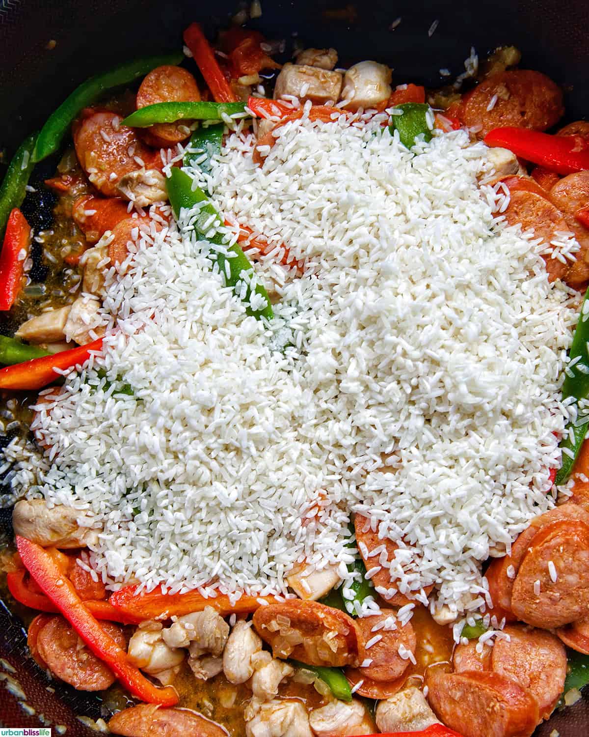 white rice added to the top of Arroz a la Valenciana in a skillet.