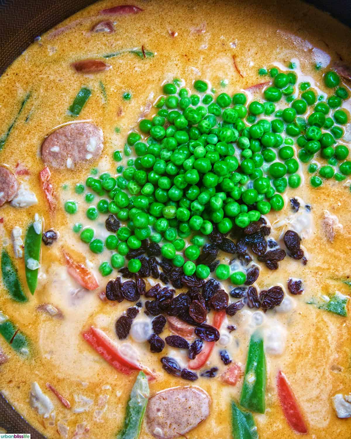 green peas and raisins added to Arroz a la Valenciana in a skillet.