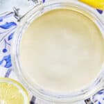 jar of lemon tahini dressing with sides of cut lemons.
