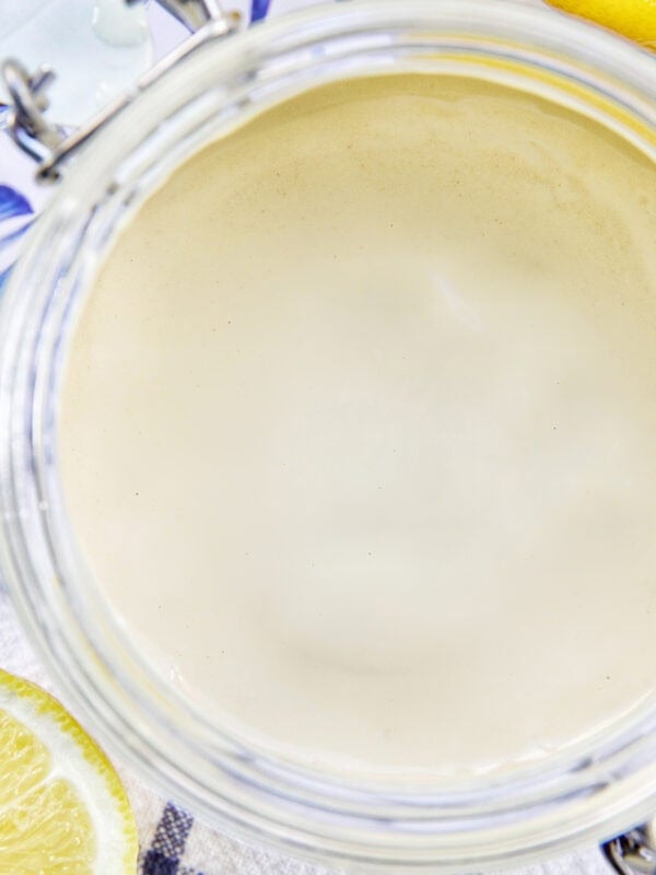 jar of lemon tahini dressing with sides of cut lemons.