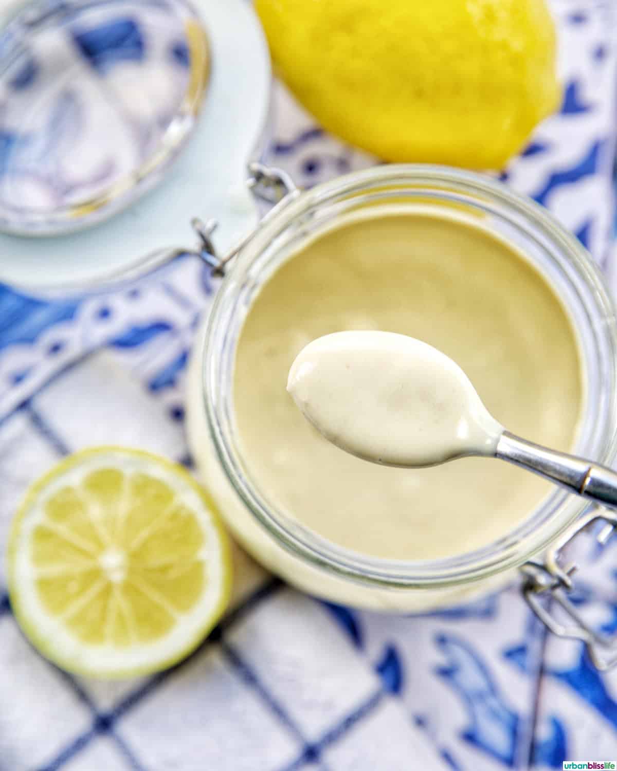 spoon of lemon tahini dressing over a jar with sides of cut lemons.