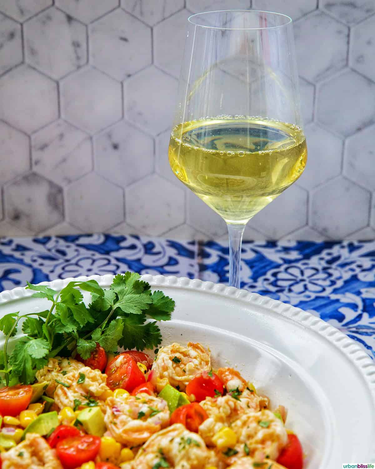glass of white wine behind a bowl of shrimp corn salad.