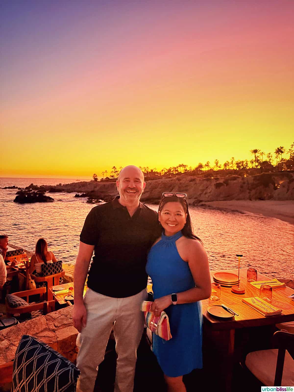 Marlynn Jayme Schotland and Alain Schotland standing with the sea and sunset in background at Cocina del Mar restaurant in Cabo San Lucas, Mexico.