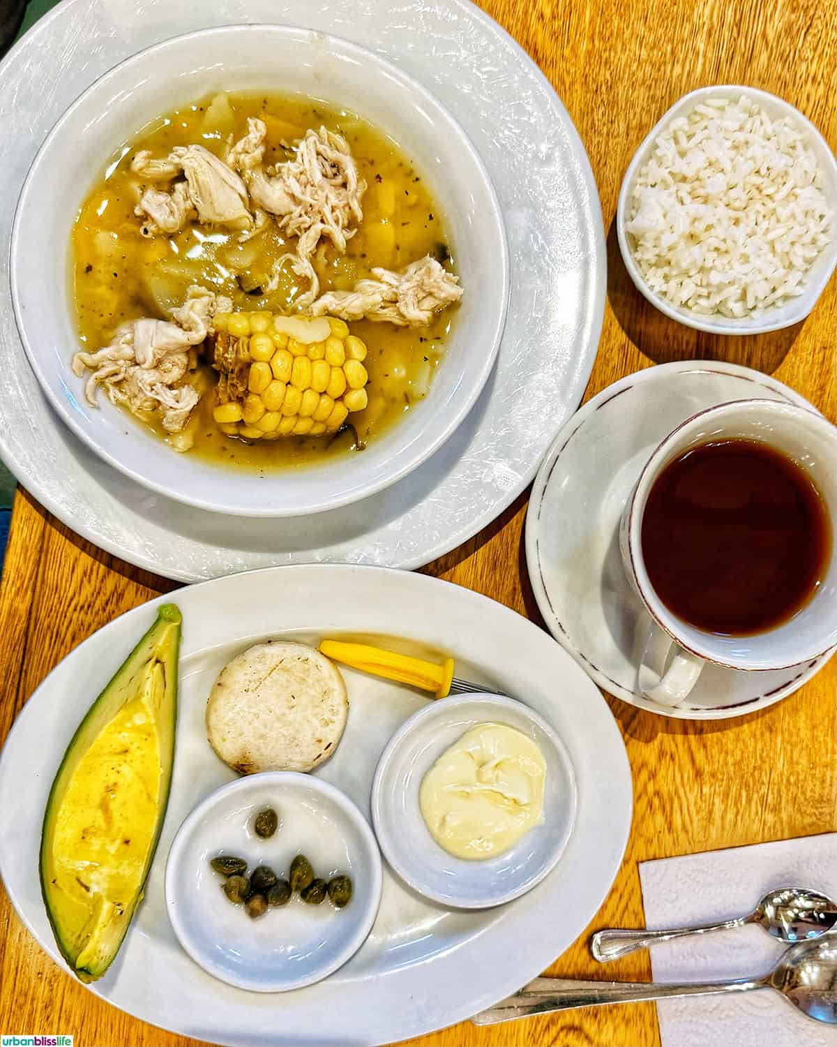 bowl of ajiaco soup with side of rice, avocado, corn, capers, sour cream in Colombia.