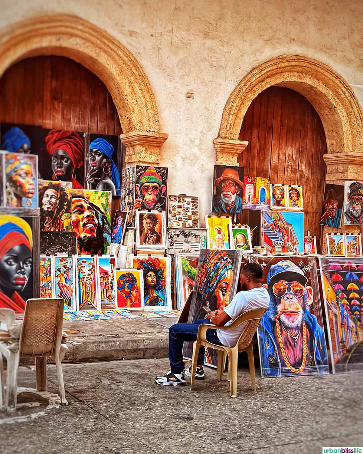 artist with several canvasses of colorful art in Cartagena, Colombia.