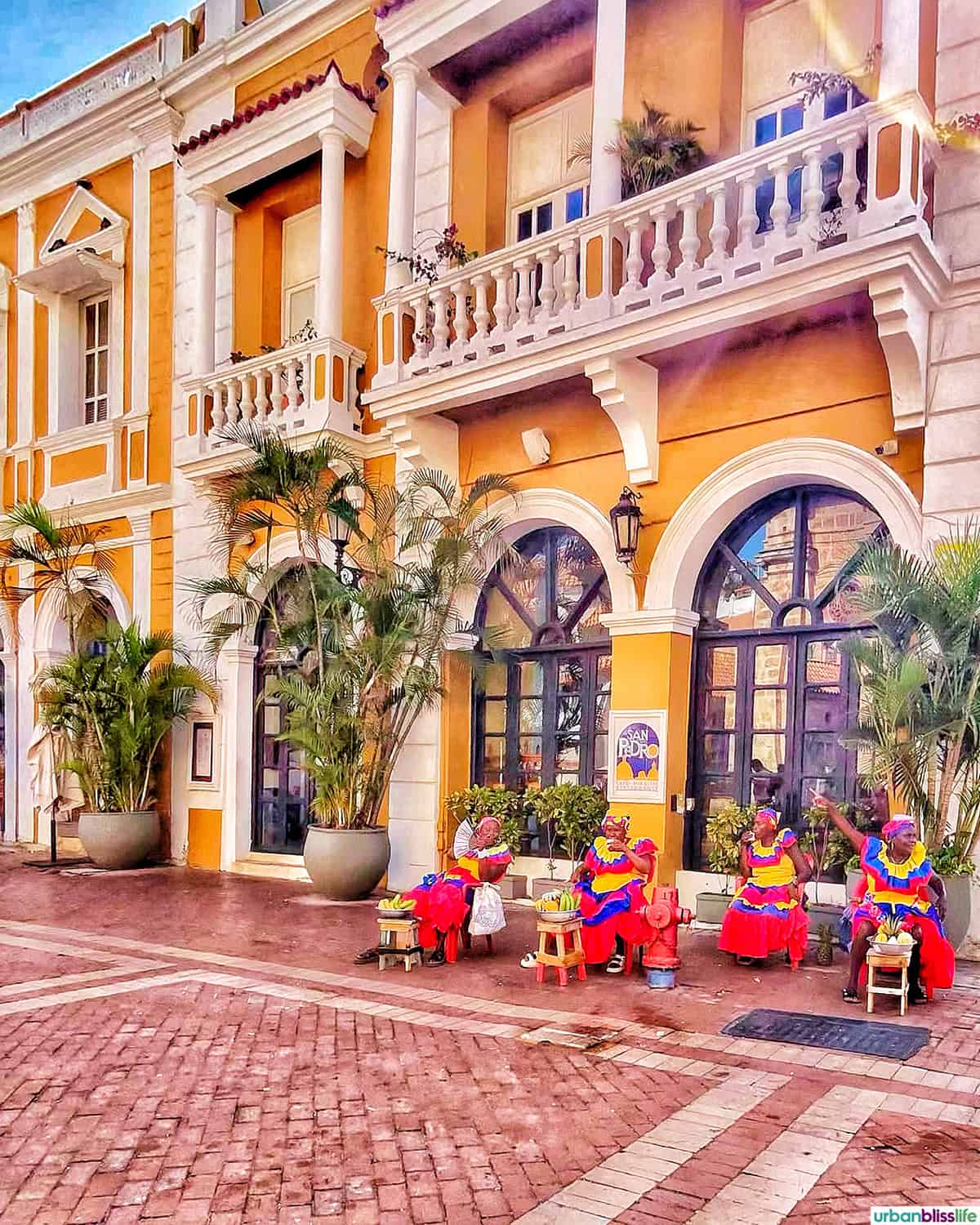 beautiful yellow building with Colombian women in red, yellow, and blue dresses.