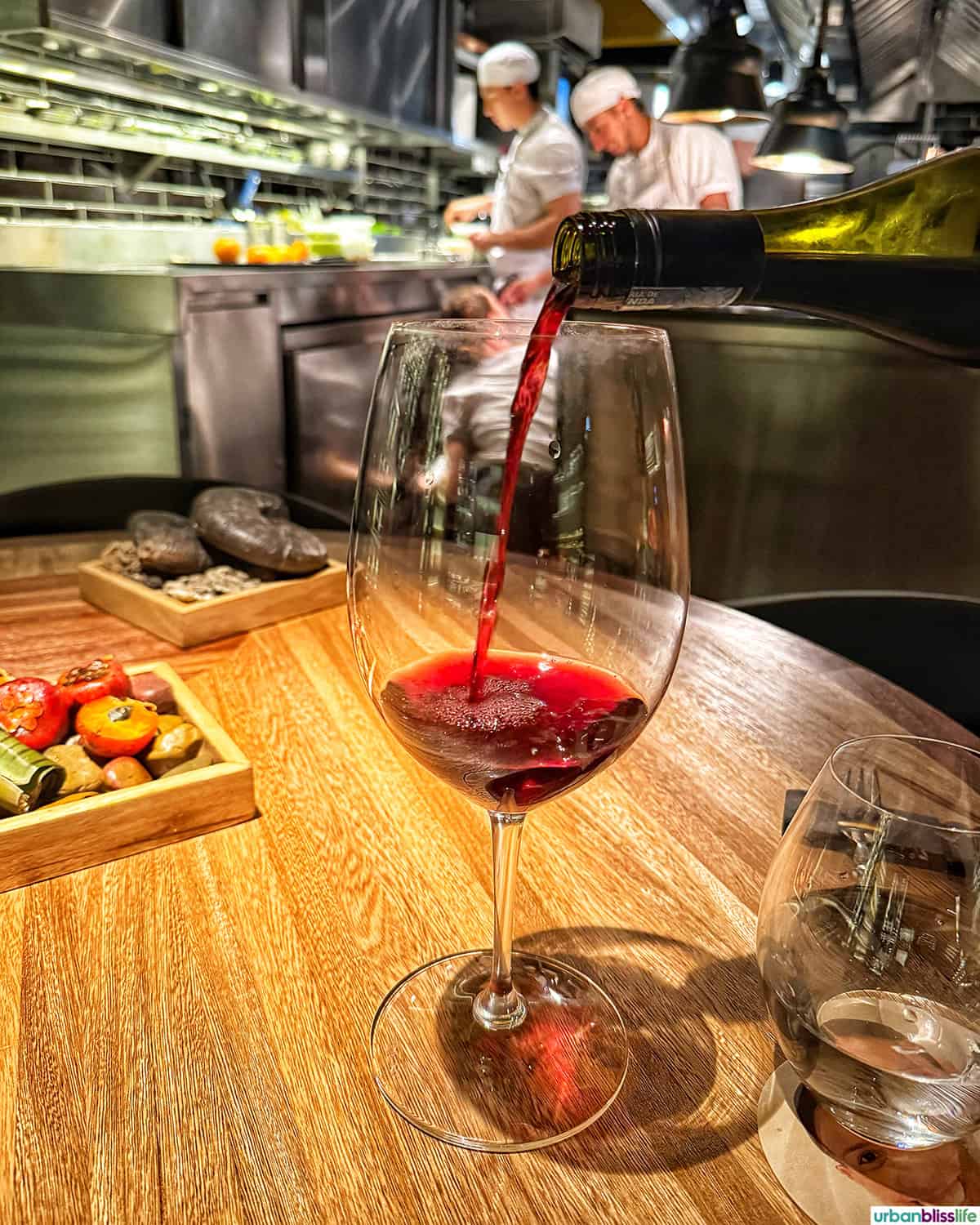pouring red wine into a glass with the kitchen in the background at El Chato restaurant in Bogota, Colombia.