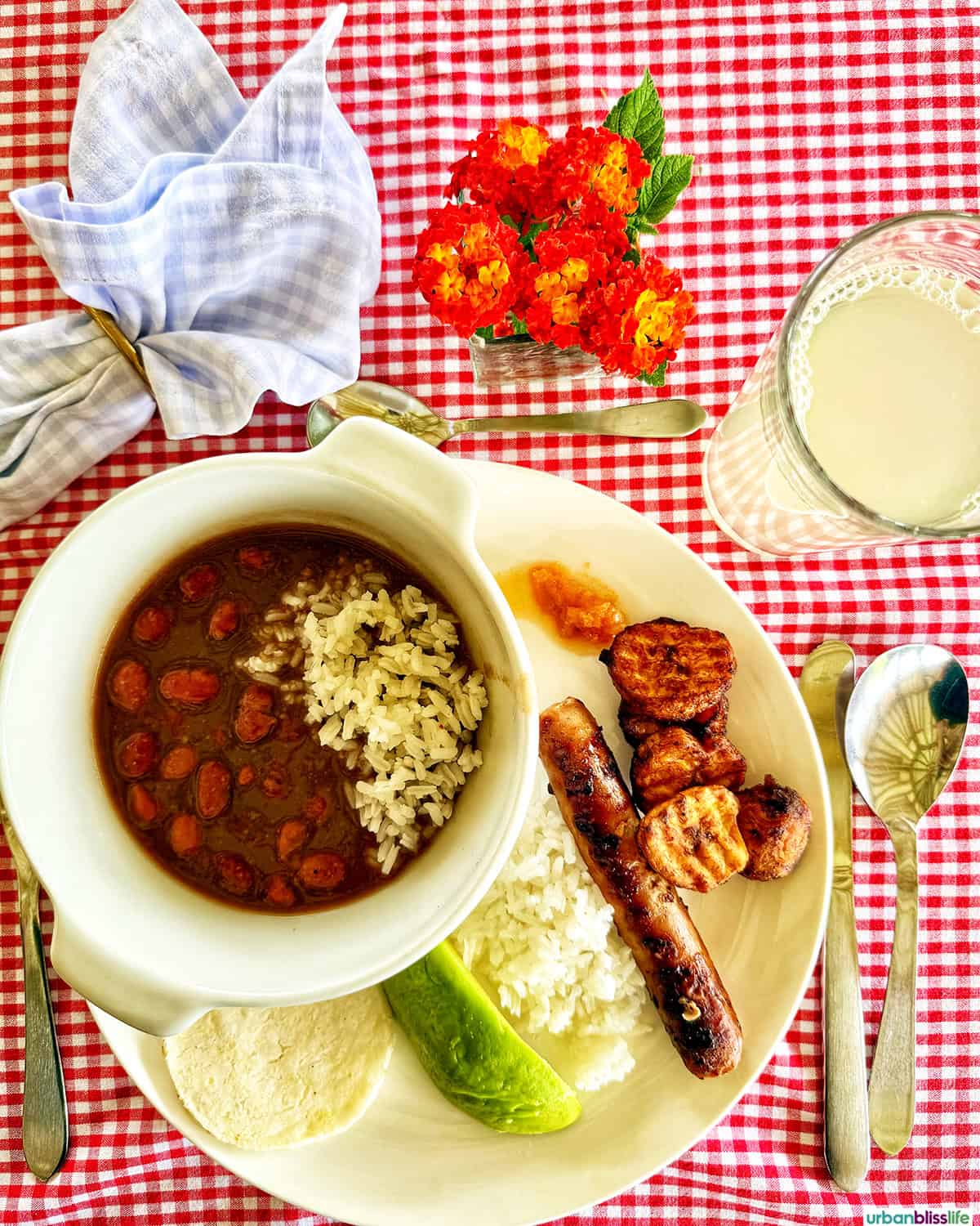 Frijolada with rice, avocado, chorizo on a red checkered tablecloth.