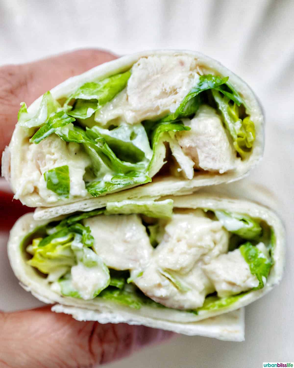 hand holding Chicken Caesar Salad Wrap sliced in half.
