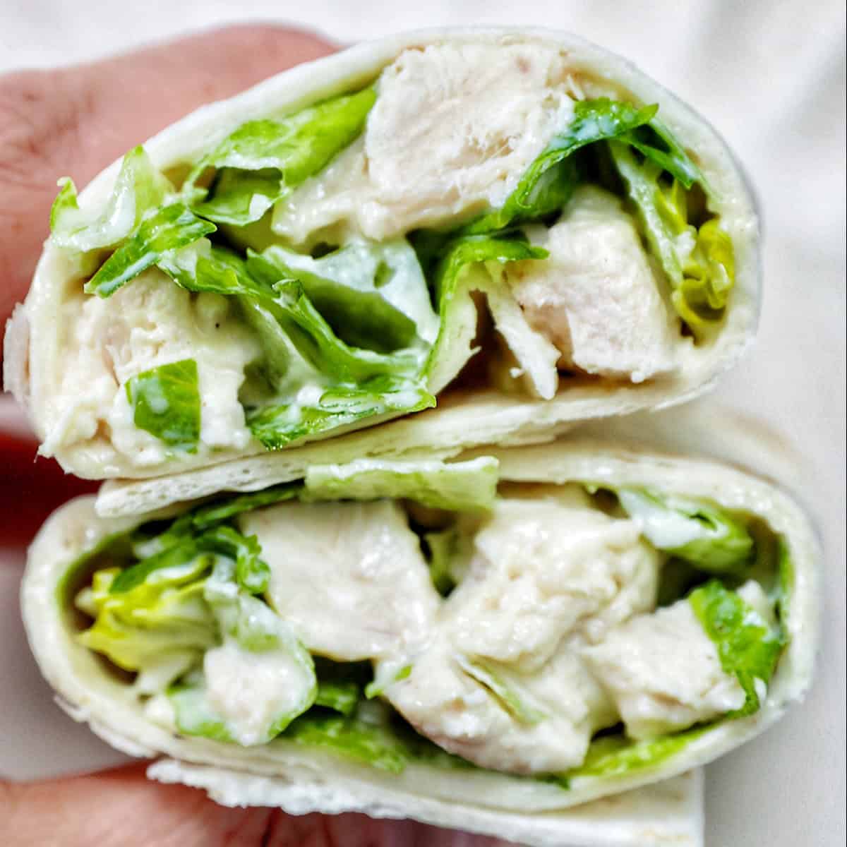 hand holding a Chicken Caesar Salad Wrap sliced in half.