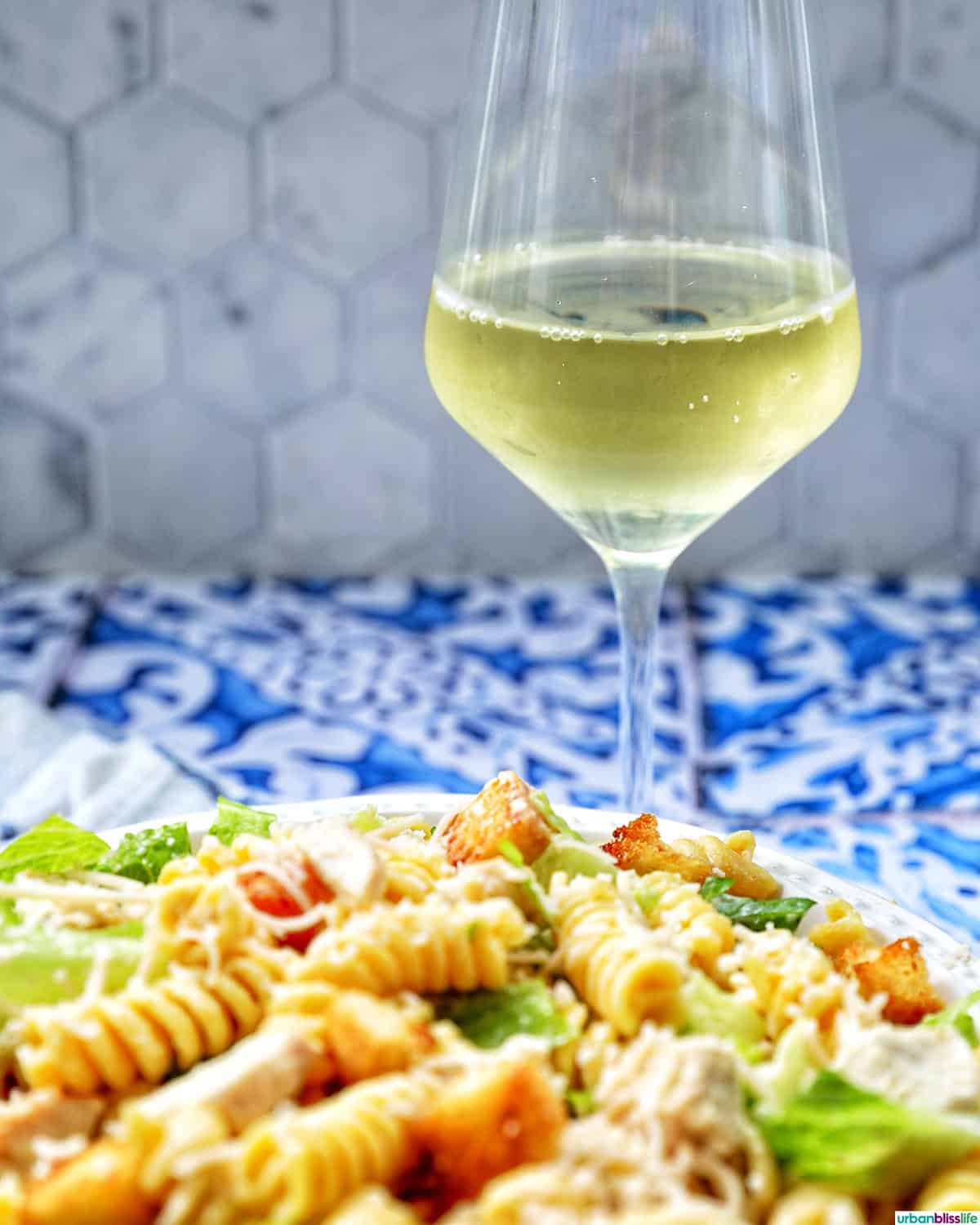 glass of white wine and bowl of Caesar pasta salad.