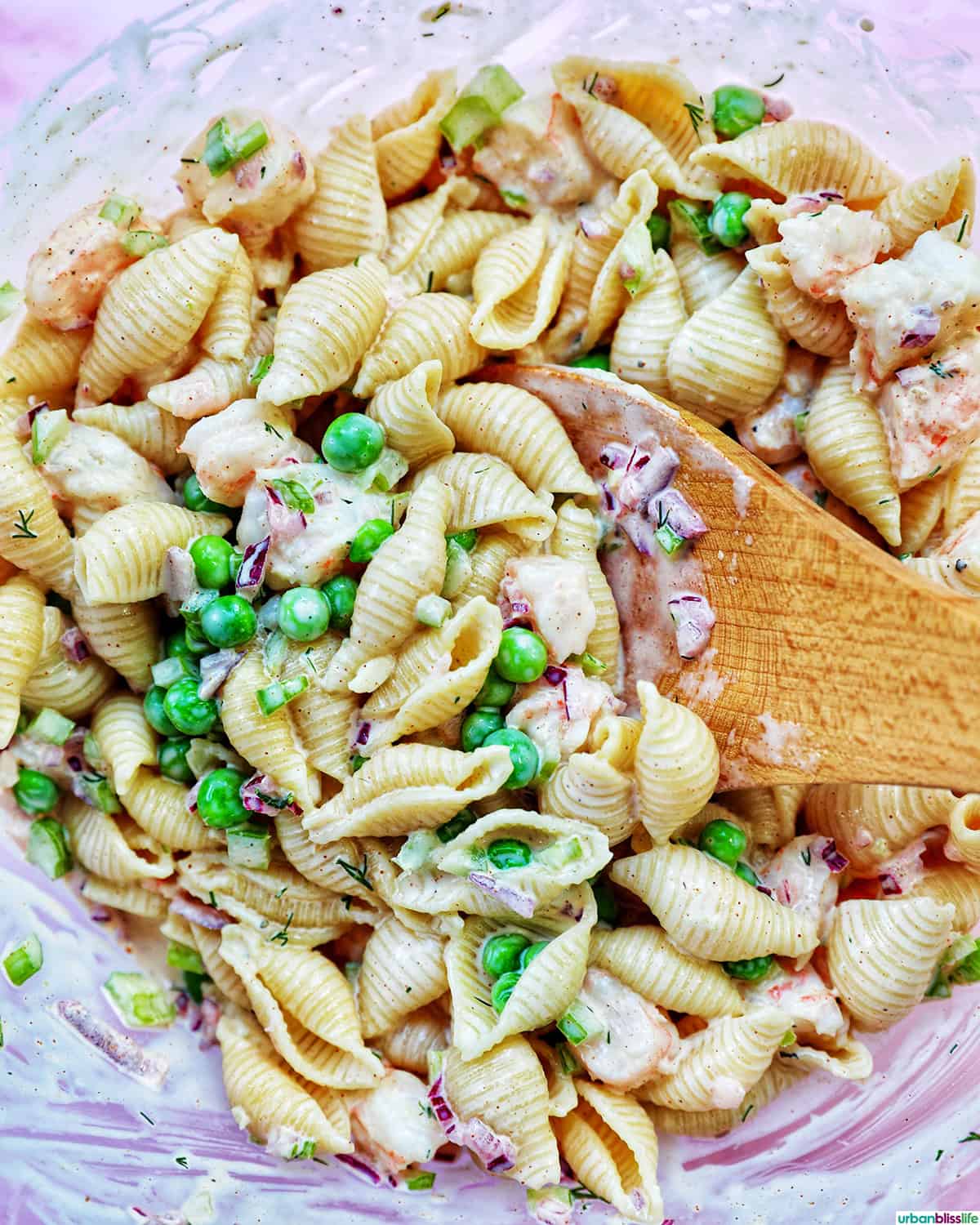 wooden spoon in a bowl of shrimp pasta salad.
