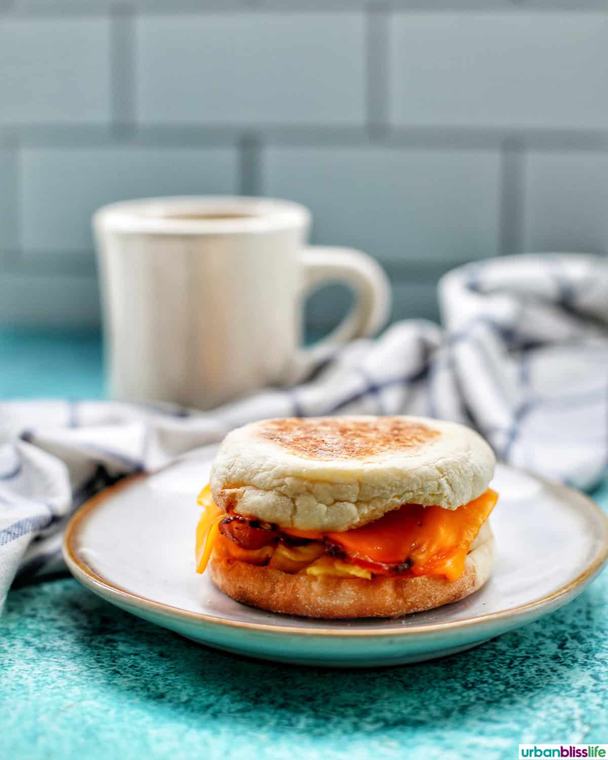 air fryer breakfast sandwich on a plate with a cup of coffee in the background.