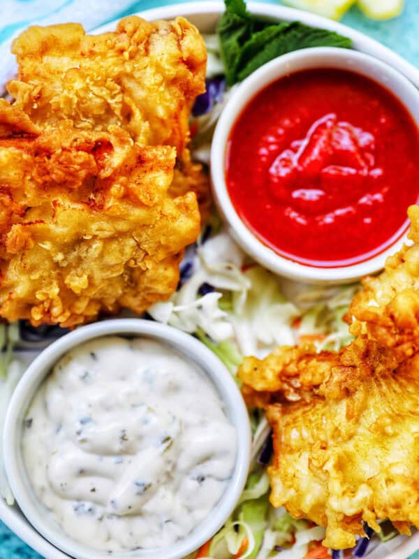 air fryer cod pieces on a plate with sides of tartar sauce, coleslaw, and cocktail sauce.