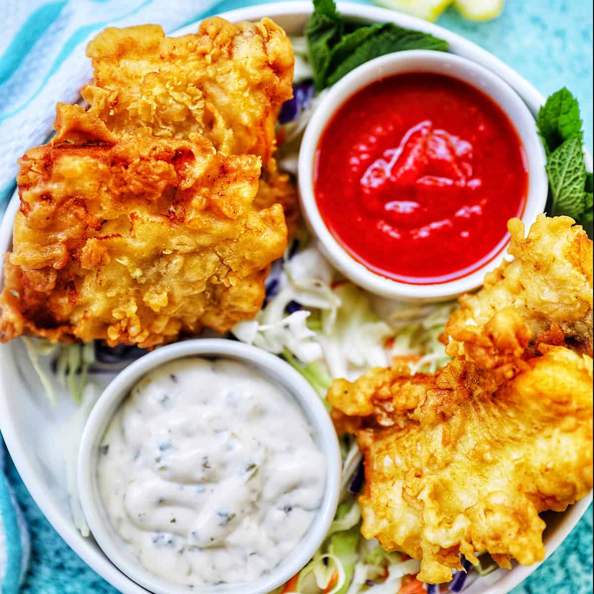 air fryer cod pieces on a plate with sides of tartar sauce, coleslaw, and cocktail sauce.